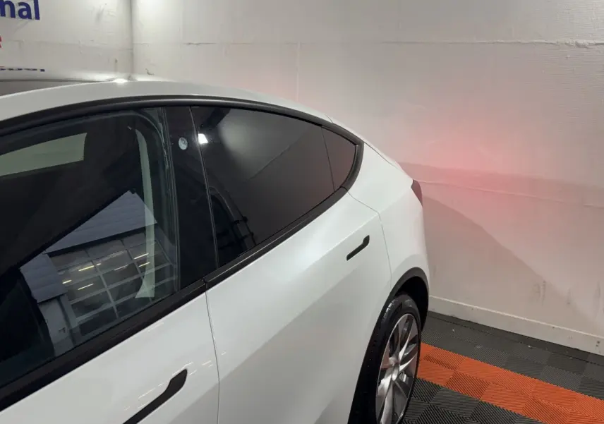 Vue 3/4 arrière droite d'une Tesla Model Y blanche avec vitres teintées et poignées affleurantes noires.
