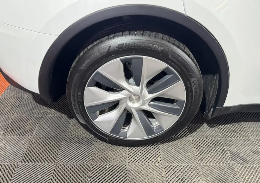 Gros plan sur la roue arrière droite d’un Tesla Model Y blanc, mettant en valeur la jante aérodynamique et le pneu Hankook.
