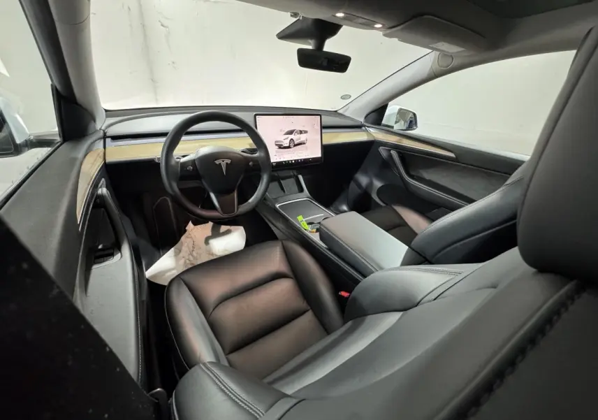 Intérieur Tesla Model Y blanc vu côté passager avant, tableau de bord épuré avec écran tactile central et sièges cuir noirs.