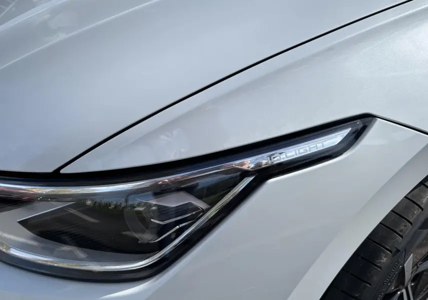 Gros plan sur le phare avant droit blanc de la Volkswagen Golf 1.5 eTSI Edition 50 2024 avec jante noire visible.