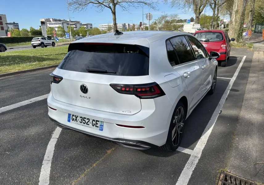 Vue 3/4 arrière droite d'une Volkswagen Golf blanche 1.5 eTSI Edition 50 2024, garée sur rue avec vitres teintées.