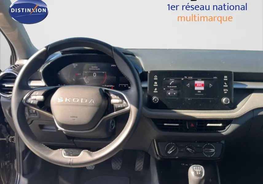 Vue intérieure centrée sur le volant Skoda noir et le tableau de bord avec écran tactile et commandes manuelles.