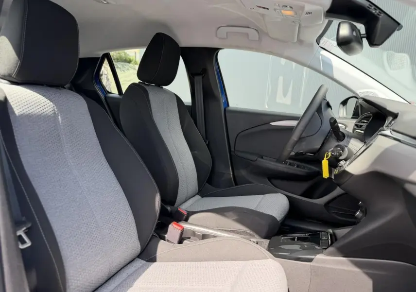 Vue intérieure côté gauche de l’Opel Corsa 2025 bleu Voltaic, montrant les sièges avant bicolores et le tableau de bord moderne.