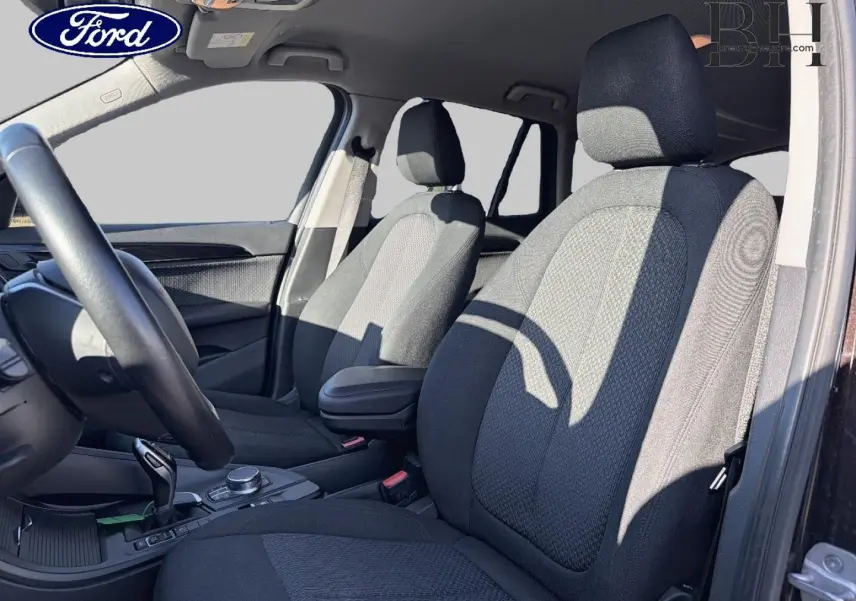 Vue intérieure avant droite du BMW X1 sDrive18dA 2018 avec sièges tissu noirs et accoudoir central.