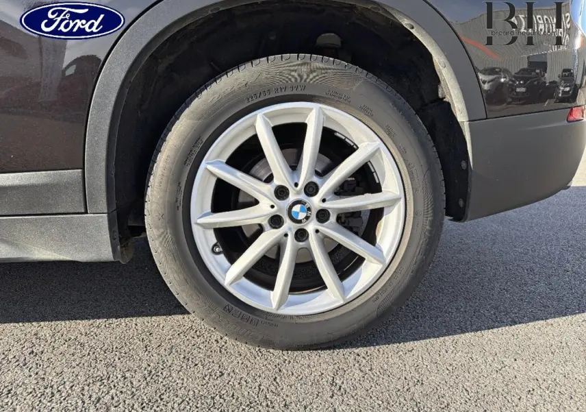Gros plan sur la roue arrière droite d’un BMW X1 sDrive18dA 2018 noir Saphirschwarz avec jante alu argentée.