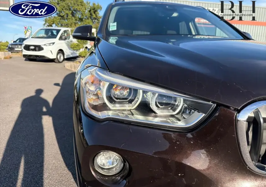 Gros plan sur l'avant gauche d'une BMW X1 sDrive18dA 2018 en Saphirschwarz, mettant en valeur le phare et la calandre.