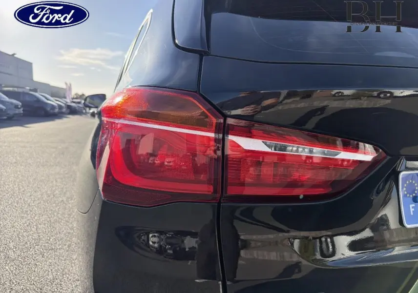 Gros plan sur le feu arrière gauche d’un BMW X1 sDrive18dA 2018 en noir Saphirschwarz, avec reflet sur la carrosserie brillante.
