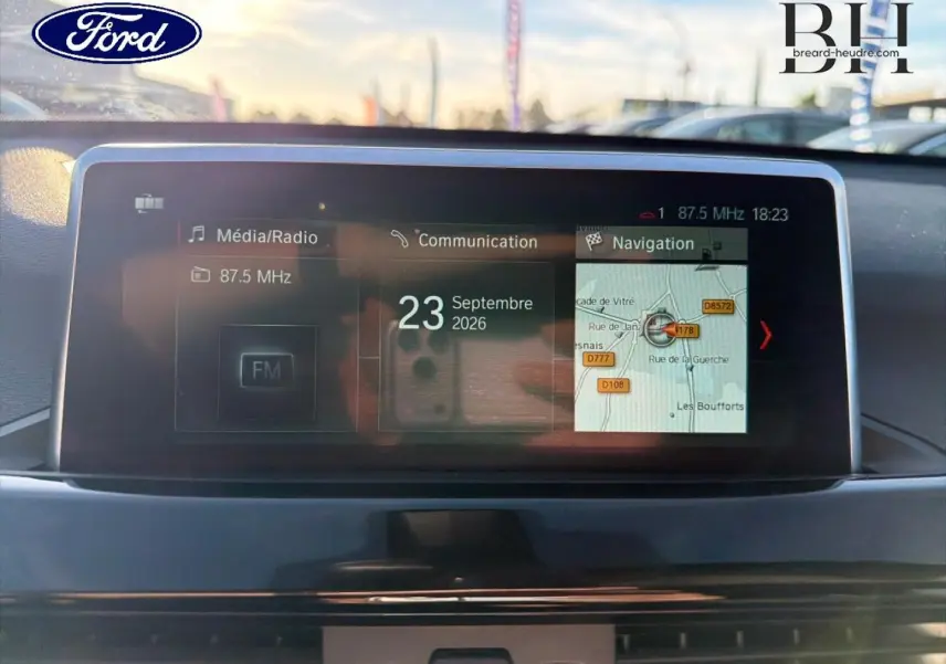 Écran multimédia central d'une BMW X1 sDrive18dA 2018, affichant radio FM et navigation, vue intérieure frontale.