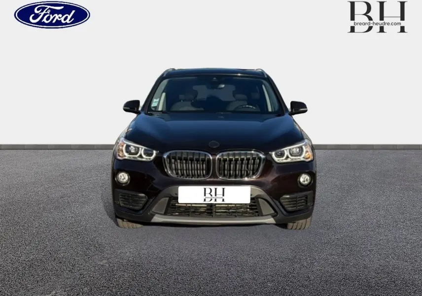 Vue de face d’un BMW X1 sDrive18dA 150ch Lounge noir Saphirschwarz avec calandre caractéristique et phares allumés.
