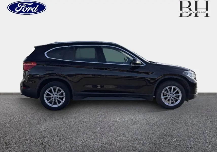 Profil droit d'un BMW X1 sDrive18dA 2018 noir saphir avec jantes alliage et barres de toit visibles.