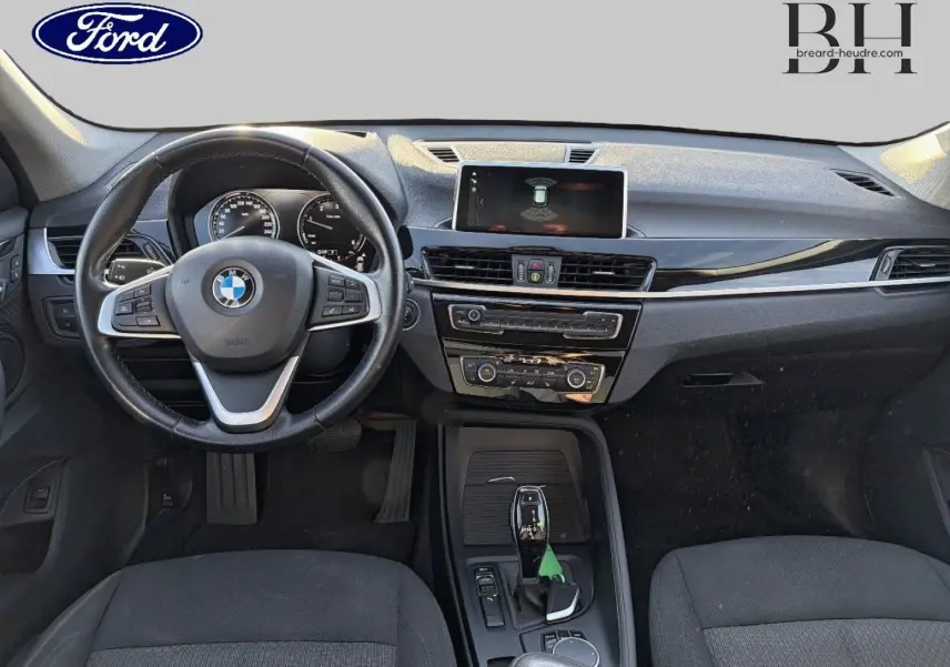 Vue intérieure avant de la BMW X1 sDrive18dA 2018 avec volant cuir multifonction et console centrale noire.