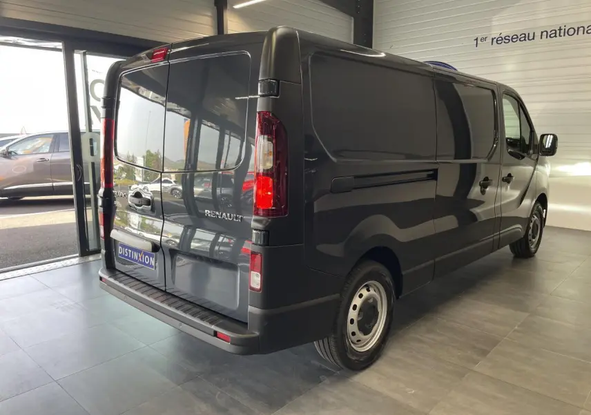 Renault Trafic Fourgon gris Comète vu en 3/4 arrière droit dans un showroom lumineux avec portes arrière fermées.