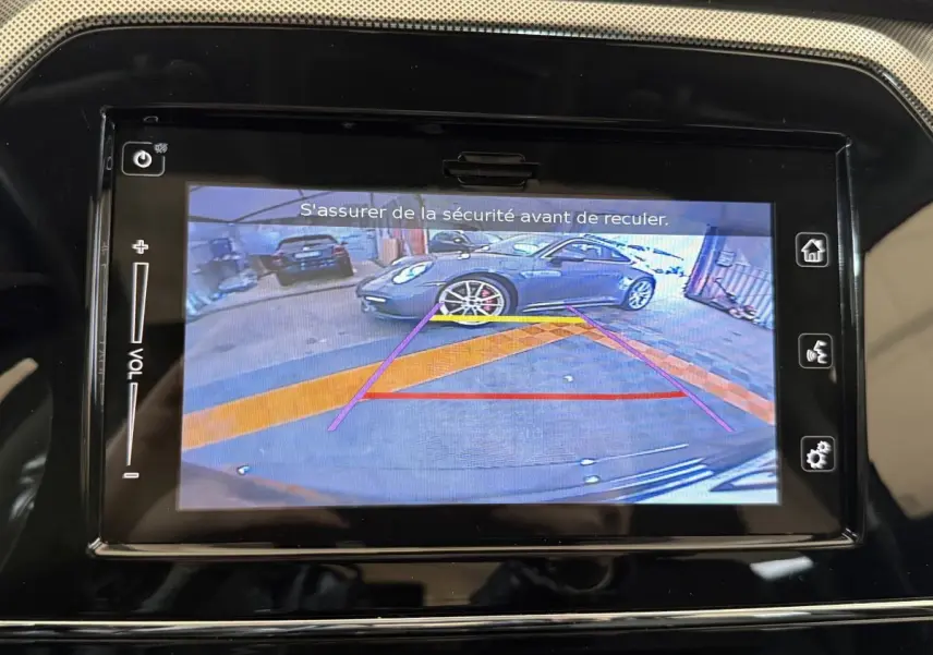Écran tactile du Suzuki Vitara 2022 montrant la caméra de recul avec vue arrière sur un véhicule gris en garage.