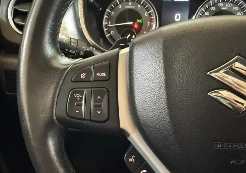 Gros plan sur le volant cuir et alu du Suzuki Vitara noir 2022, avec commandes audio et affichage du tableau de bord en arrière-plan.