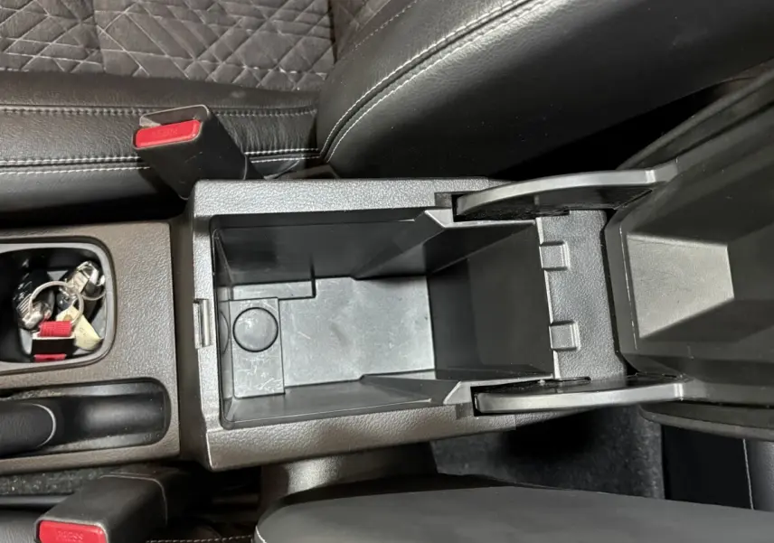 Vue plongeante sur le rangement central ouvert du Suzuki Vitara noir, avec siège et ceinture visibles.