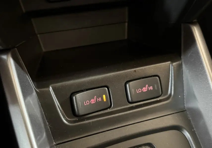 Gros plan sur les boutons de chauffage des sièges avant du Suzuki Vitara noir, avec témoin lumineux allumé à gauche.