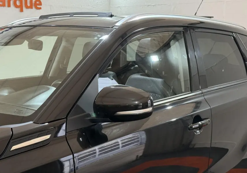 Vue latérale côté gauche d’un Suzuki Vitara noir avec rétroviseur et poignées de porte chromées, intérieur visible.