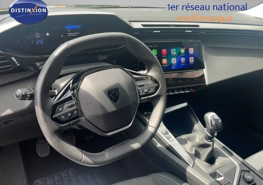 Intérieur de Peugeot 308 2024, vue du poste de conduite avec volant compact et levier de vitesses manuel, ambiance gris noir.