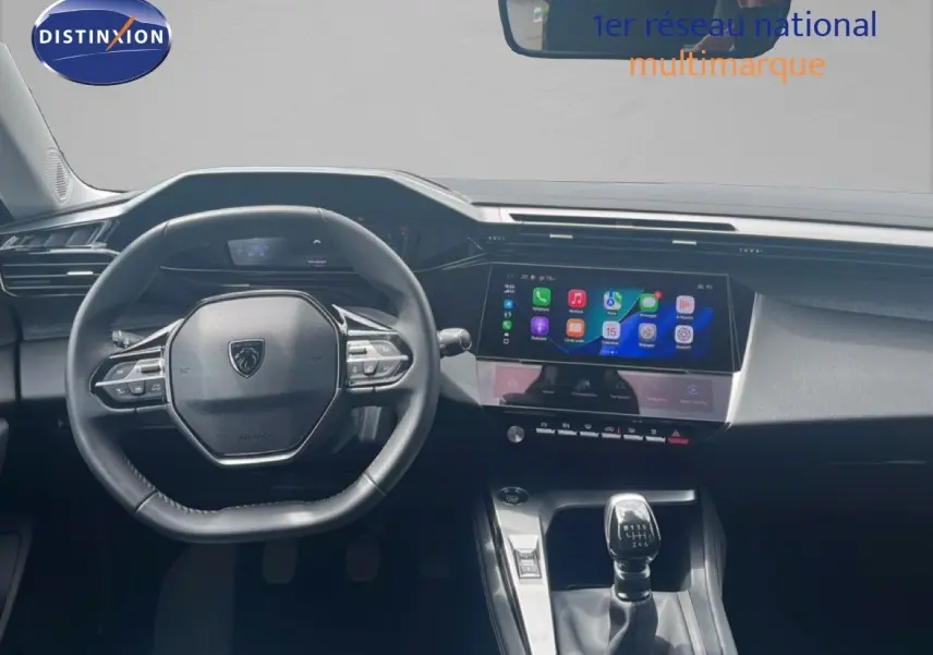 Vue intérieure centrée sur le volant Peugeot et la console centrale avec écran tactile et levier de vitesse manuelle.