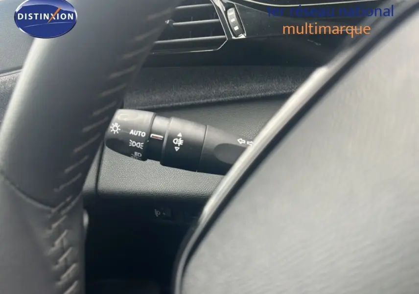 Gros plan sur la commande des phares à gauche du volant dans l’habitacle gris noir d’une Peugeot 308 2024.