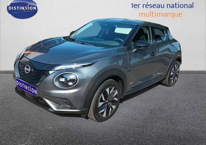 Nissan Juke Hybrid gris squale métal en 3/4 avant droit, avec calandre noire et jantes bicolores distinctives.
