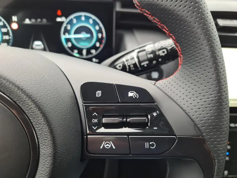 Gros plan sur les commandes du volant N-LINE cuir perforé du Hyundai Tucson IV blanc polaire, avec tableau de bord numérique en arrière-plan.