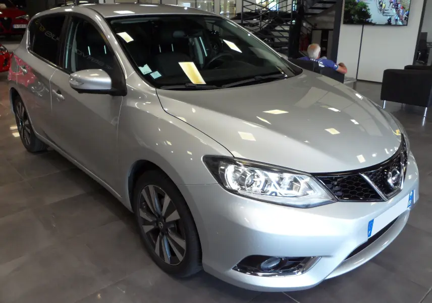 Nissan Pulsar gris glacier vue 3/4 avant droit en showroom, mettant en valeur ses phares et jantes alliage.