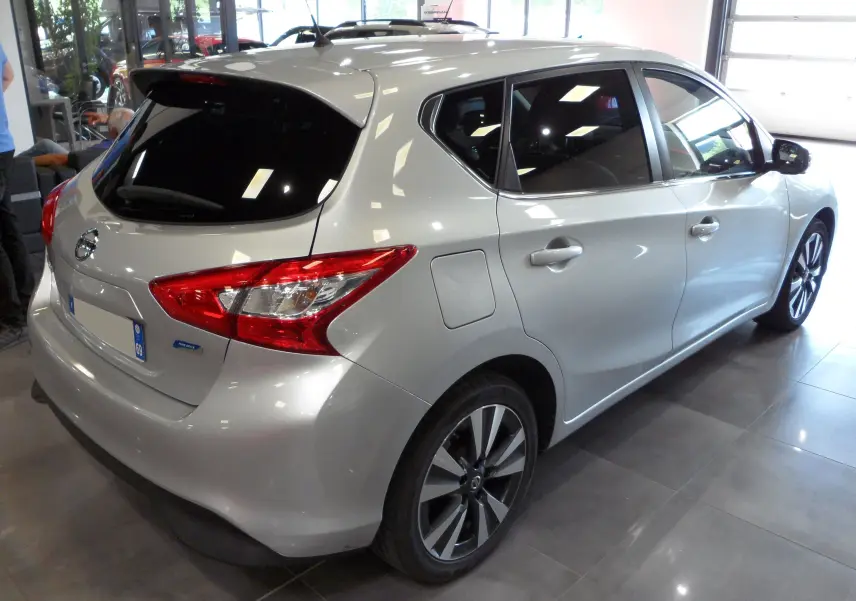 Vue 3/4 arrière droite d'une Nissan Pulsar gris glacier avec jantes alliage et vitres teintées en intérieur showroom.