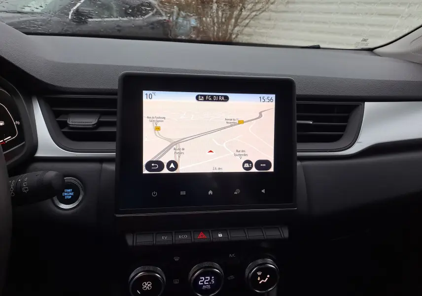Vue intérieure centrée sur l’écran tactile du tableau de bord du Renault Captur gris, avec commandes climatisation et bouton start visible.