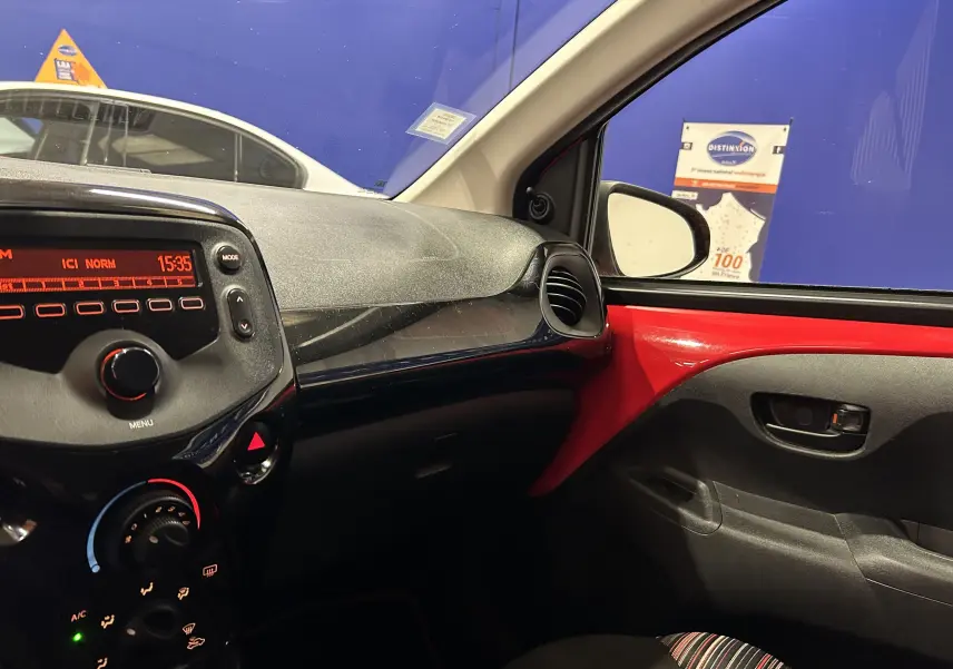 Intérieur côté passager d'une Citroën C1 rouge 2019, tableau de bord et porte avec détails rouges visibles.