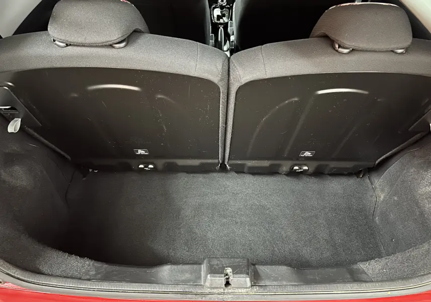 Vue plongeante sur le coffre ouvert d'une Citroën C1 rouge, montrant l'espace de rangement et le dos des sièges arrière.