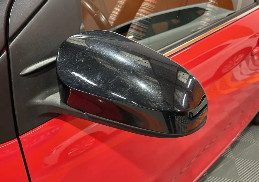 Rétroviseur noir en gros plan côté gauche d'une Citroën C1 Airscape rouge, avec reflet de l'environnement intérieur.