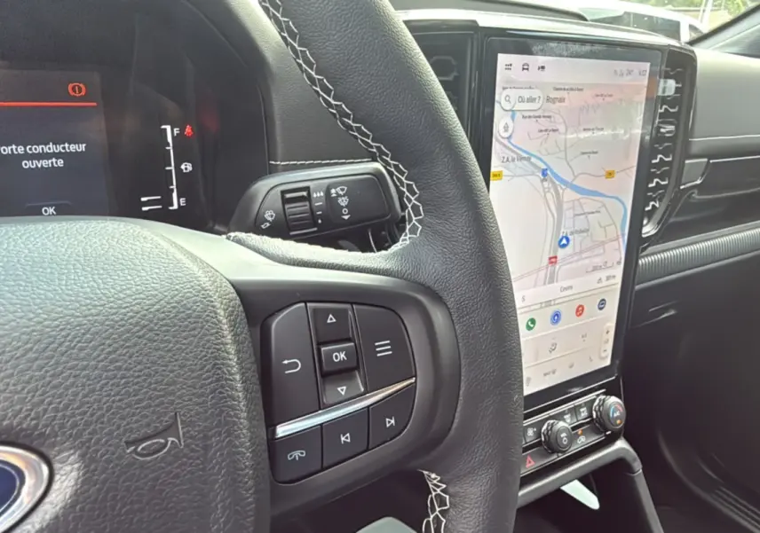 Intérieur du Ford Ranger 2025 noir agate, vue rapprochée du volant avec commandes et écran tactile vertical affichant la navigation.