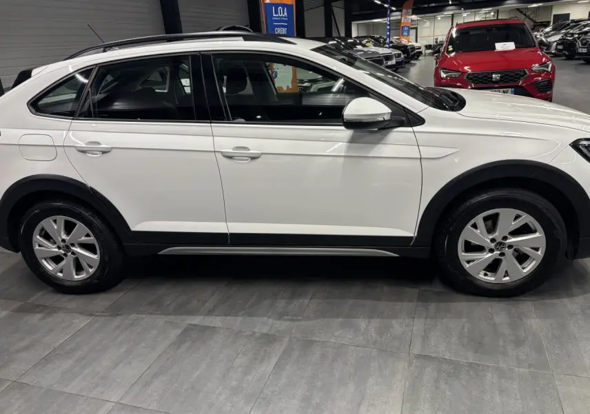 Vue de profil côté droit d'un Volkswagen Taigo blanc avec jantes alliage et protections noires sur les passages de roues.