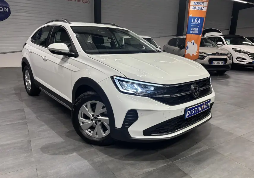 Volkswagen Taigo blanc en 3/4 avant droit, avec jantes alliage et phares LED allumés en intérieur showroom.