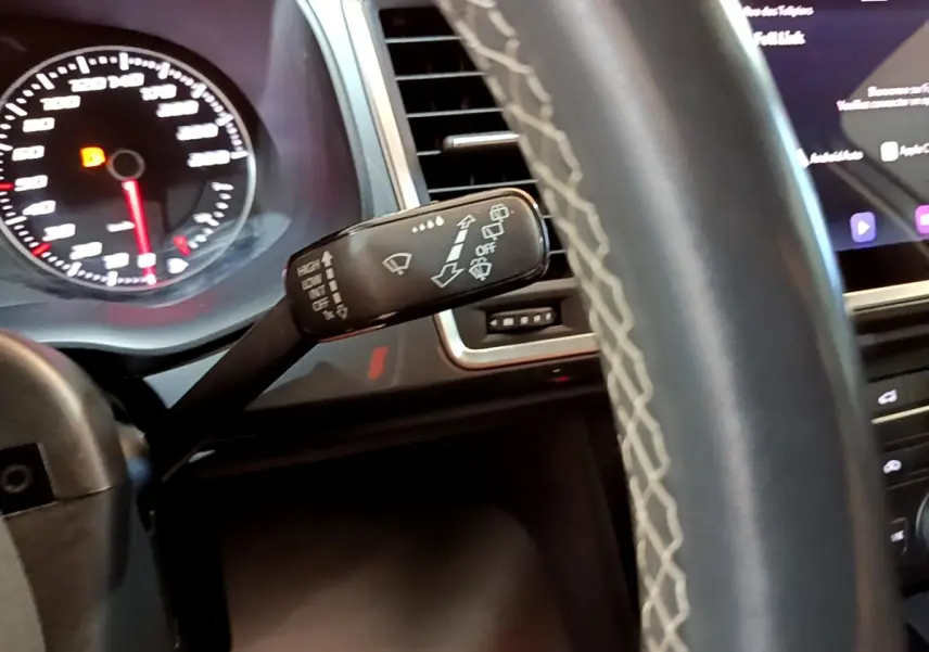 Vue rapprochée du commodo d’essuie-glace à gauche du volant cuir gris du SEAT Ateca 2022, tableau de bord et écran tactile visibles.