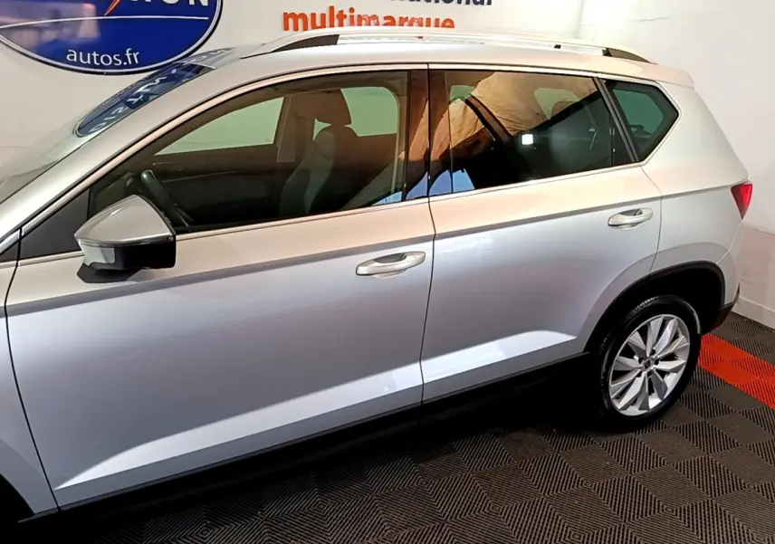 Vue de profil côté gauche du SEAT Ateca gris clair 2022 avec jantes alliage et barres de toit chromées.