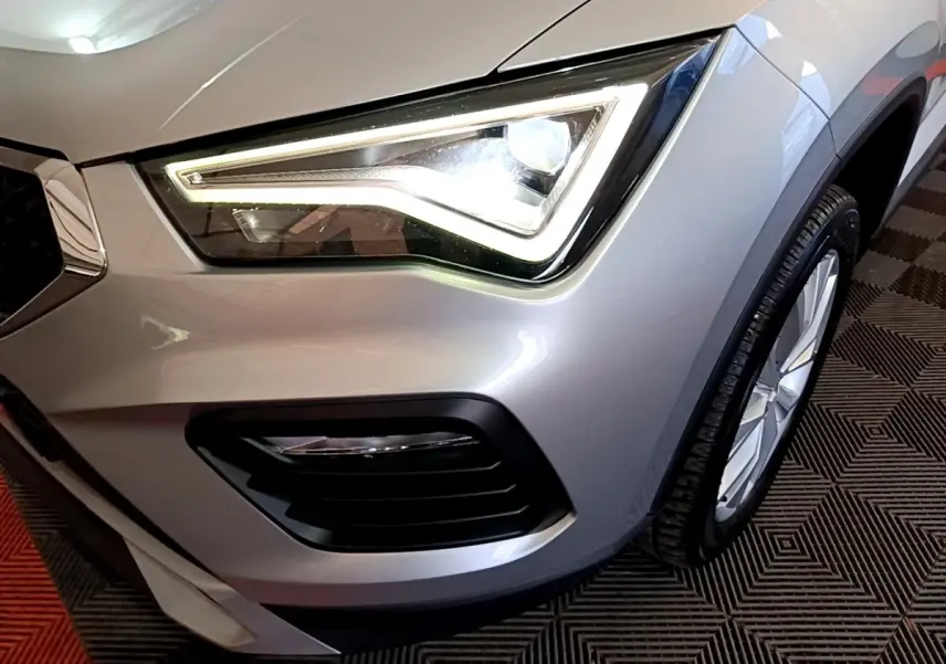 Gros plan sur le phare avant droit allumé d’un SEAT Ateca gris clair, avec partie de la roue visible.