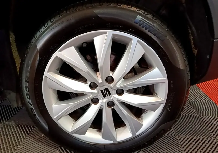 Gros plan sur la jante alliage argentée avec logo SEAT, montée sur pneu Pirelli, véhicule gris clair visible en arrière-plan.