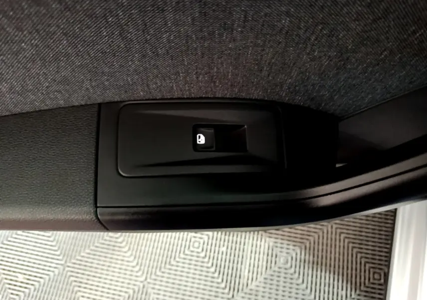 Gros plan sur le bouton d'ouverture électrique du coffre, situé sur le côté intérieur d'une SEAT Ateca gris clair.