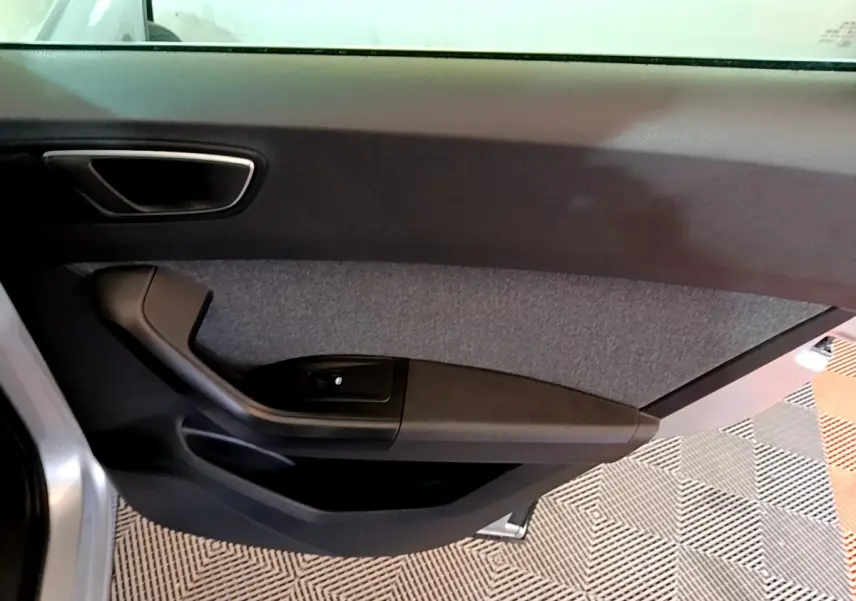 Vue intérieure de la porte côté gauche d’un SEAT Ateca gris clair, avec poignée noire et garniture textile grise.