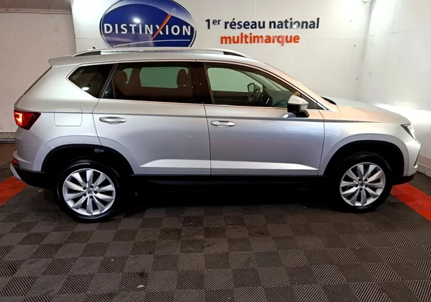 Vue latérale droite d'un SEAT Ateca gris clair 2022 dans un showroom avec logo Distinxion en arrière-plan.