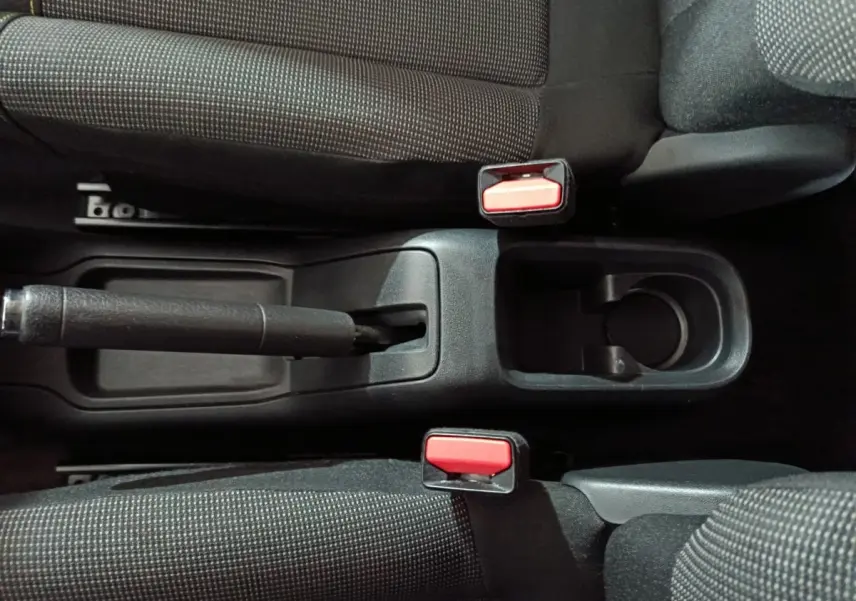 Vue plongeante sur la console centrale noire de la Citroën C3 2024 avec frein à main manuel et deux ceintures rouges.