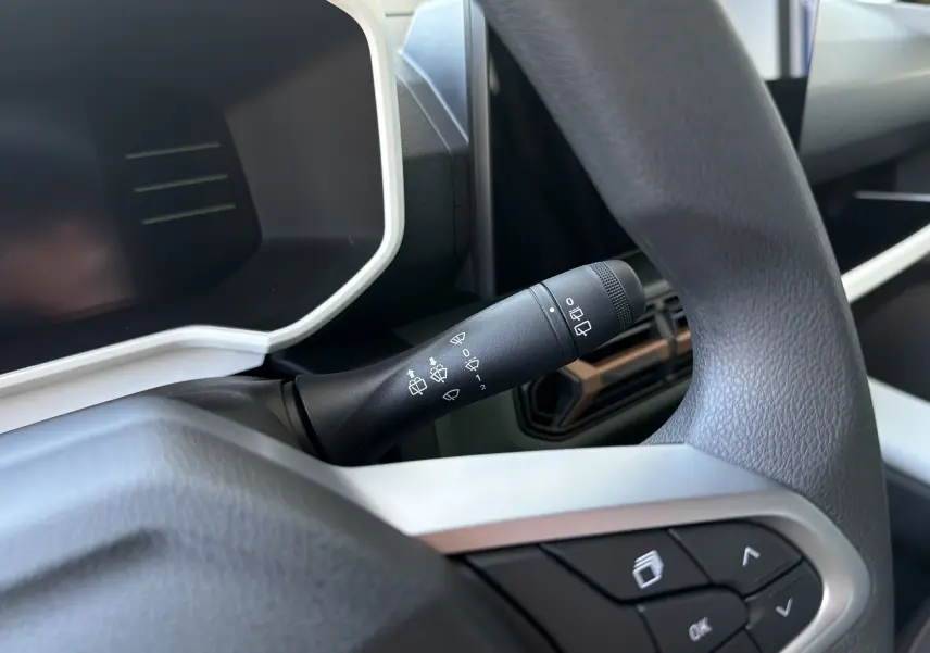 Gros plan sur la commande d’essuie-glace à gauche du volant noir dans l’habitacle du Dacia Spring Beige Safari 2026.