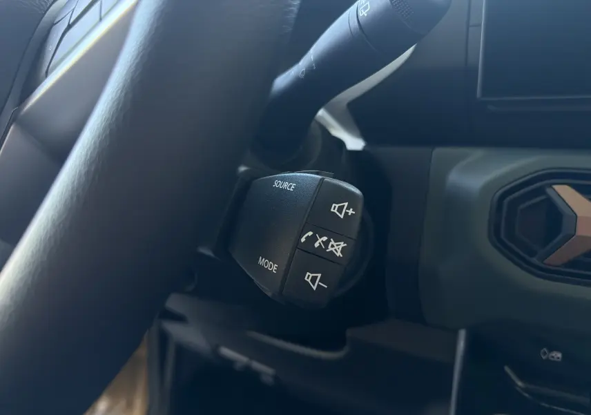 Gros plan sur les commandes au volant du Dacia Spring 65 Extreme 2026, intérieur noir avec détails beige safari visibles.