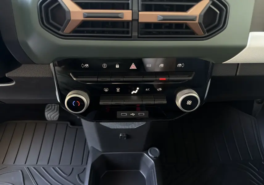 Vue rapprochée de la console centrale de la Dacia Spring 65 Extreme 2026 beige Safari, avec commandes climatisation et prises USB.