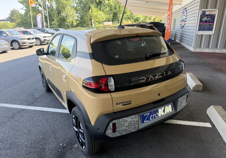 Vue 3/4 arrière droite d'une Dacia Spring 65 Extreme beige Safari avec logo DACIA noir brillant et plaque Zéro KM.