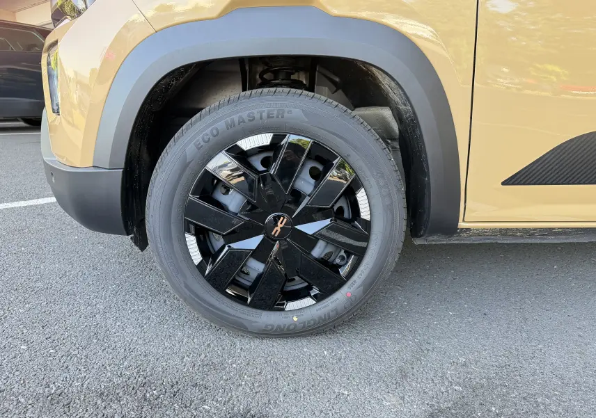 Gros plan sur la roue avant droite du Dacia Spring 65 Extreme beige Safari, avec jante noire brillante et détails modernes.