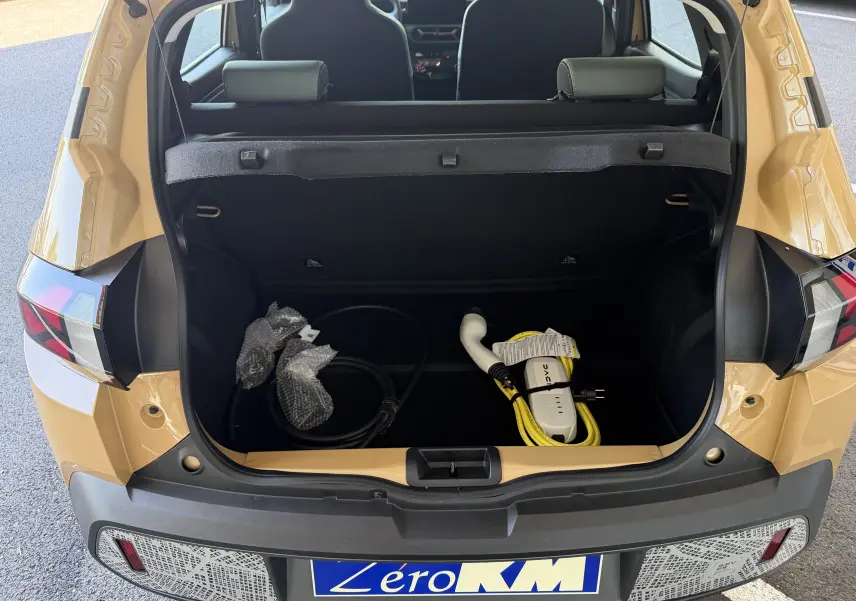 Vue arrière ouverte du coffre beige safari du Dacia Spring 65 Extreme 2026, avec câble de recharge électrique visible.