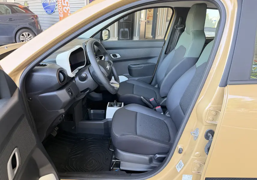 Vue intérieure côté conducteur de la Dacia Spring 65 Extreme beige Safari 2026, avec sièges noirs et tableau de bord moderne.